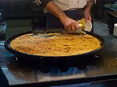 Grande et fine galette cuite de couleur jaune orangée au sortir du four en train d'être servie sur sa plaque.