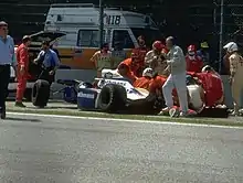 Photo des secours au chevet d'Ayrton Senna. L'arrière de sa monoplace, bleue et blanche, est totalement détruit.