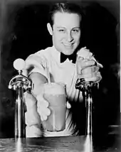 Un "soda jerk" servant un soda à la crème glacée. Sa main gauche repose sur le robinet d'une fontaine à soda (1936)