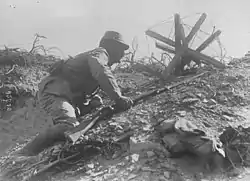 Photographie d'un soldat rampant hors d'une tranchée avec un fusil à la main