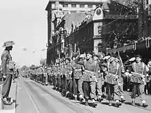 Photo en noir et blanc de soldats marchant en formation serrée dans une rue.