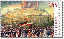 Le timbre reprend le tableau précédent concernant la fête de Hambach, en couleur cette fois. D'autres drapeaux se trouvent à côté de celui allemand.