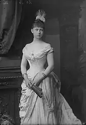 Photographie en noir et blanc d'une jeune femme portant une robe décolletée et tenant dans ses mains un évantail.