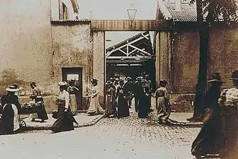 Sortie de l'usine Lumière, 1895. L'image fixée de l'usine, ici de son portail et un de ses hangars, un atelier de chapellerie reconverti, pour la fabrication de plaques photo, fait partie du patrimoine industriel.