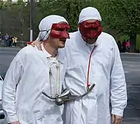 Deux Soufflaculs sont vêtus de chemises de nuit blanches et de bonnets de coton blanc et portent des masques rouges.