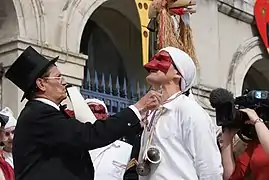 Un homme à lunettes, habillé d'un haut-de-forme et d'une queue-de-pie, distingue un Soufflacul avec un sautoir tricolore (bleu, blanc et rouge) sur lequel est attachée une sardine.