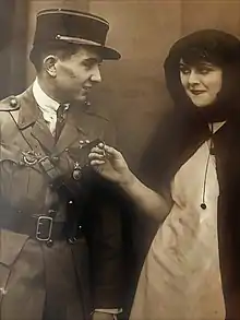 Constant Soulier, en uniforme, à gauche, regarde dans les yeux une jeune fille vêtue d'une sorte de cape, qui tient dans sa main la Croix de Guerre accrochée à la veste d'uniforme de Soulier.