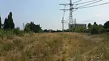 Vue de la voie ferrée (envahie par la végétation) de la ligne de Vias à Lodève, à proximité de son début, et du bâtiment de la sous-station alimentant la ligne de Bordeaux à Sète.