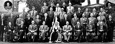 Photographie d'un groupe d'une trentaine d'hommes en costumes assis et debout sur quatre rangs