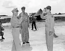 Un homme en tenue de vol salue un homme un uniforme devant plusieurs photographes.