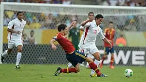 Deux footballeurs en maillot rouge et un footballeur en maillot blanc