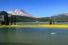 Une étendue d'eau entourée d'une forêt de conifères et, en arrière-plan, une montagne légèrement rougeâtre.