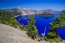 Remparts cernant un lac aux eaux bleu profond avec un cône volcanique en son sein.