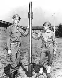 Deux soldats en uniforme américain tiennent un long projectile fin plus haut qu'eux avec des ailerons à sa base