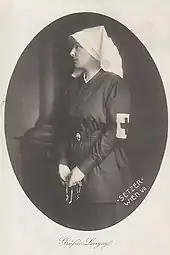 Photographie en noir et blanc, sertie dans un cadre ovale, montrant Stéphanie de profil, coiffée d'une voilette blanche, brassard de la croix-rouge au bras gauche et tenant un chapelet entre les mains.
