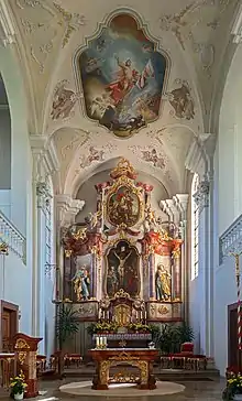 Extrémité d'une salle haute et voutée, prolongée par des tableaux magnifiant l'épopée des saints. Au bas une forte table, au milieu d'un cercle, surmontée de nombreux chandeliers.