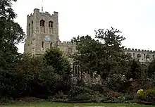 Photo d'une église en pierre grise entourée d'arbres, avec une grande tour carrée