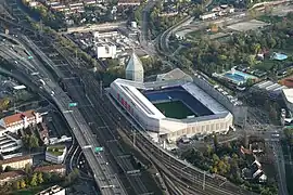 Vue aérienne d'un stade de football portant l'inscription « BASEL.CH » entouré de bâtiments, de voies de chemin de fer et d'une autoroute