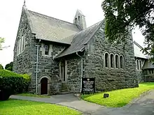 Une petite église en pierre grise, entourée d'arbres et de pelouses.