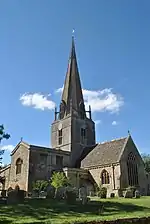 Église de pierre grise, au clocher pointu, sur fond de ciel bleu.