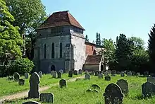 Photo d'un bâtiment muni d'une grande tour carrée au milieu d'une pelouse où s'alignent des pierres tombales