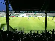 Stade de football avec plusieurs joueurs dedans, sous un ciel nocturne.