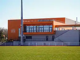 Vue d'un bâtiment orange en forme de pavé en arrière-plan, et d'un terrain en avant-plan.