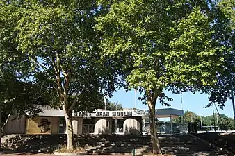 Photographie en couleur de l'entrée d'un stade, bordée d'arbres.