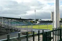 Stade de football vu de l'intérieur, avec tribune et poteau d'éclairage opposés visibles.