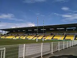 Photographie d'un terrain de rugby, avec vue sur une tribune jaune et noire