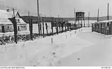 Photo noir et blanc de barbalés, d'un mirador et de baraques dans la neige