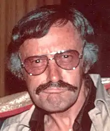 Portrait photographique d'un homme moustachu âgé d'une cinquantaine d'années, faisant une grimace.