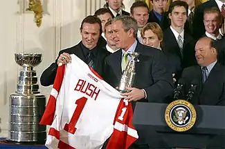 Photo de Yzerman à côté de la Coupe Stanley et qui remet à George W. Bush un maillot des Red Wings avec le numéro 1 et son nom.