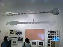 maquette d'une long vaisseau spatial  tubulaire suspendu dans une salle d'exposition au-dessus de photos de tournage.