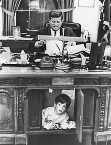 Le président John F. Kennedy travaillant à son bureau alors que son fils joue à ses pieds en 1962.