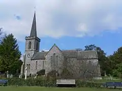 Photo d'un bâtiment en pierre grise flanqué d'une tour à la flèche élancée