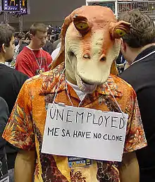 Homme avec un masque orange du personnage de Jar Jar et une pancarte où il est écrit : Unemployed, me sa have no clone.