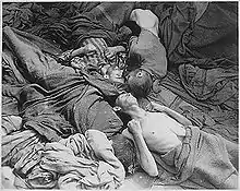 Photo noir et blanc prise dans le camp de Dachau, le 30 avril 1945. D’un fatras de couvertures de différentes nuances de gris, émergent, au centre de la photo, quatre corps décharnés de prisonniers morts de faim. Trois des têtes visibles se rejoignent au centre de la photo.