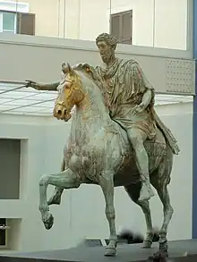 Statue d'un homme sur un cheval, tendant le bras droit en avant, de couleur grise et dorée.