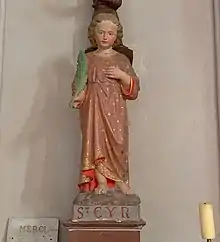 Statue d'un enfant aux cheveux châtains portant un vêtement rouge et portant une feuille dans sa main droite. Sur le socle est inscrit Saint-Cyr.