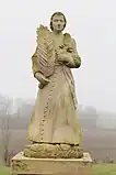 Statue montrant un homme en soutane, tenant dans sa main droite une palme et une croix dans la main gauche.