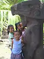 Des enfants se tiennent devant une idole de pierre précolombienne.