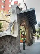 Statue d'Antoni Gaudí devant une grille et un portail de sa création.