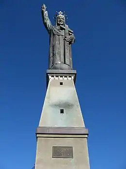 Statue en métal sur un socle en béton d'un homme qui lève le bras droit.