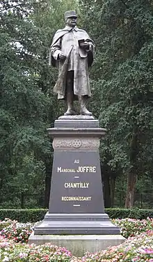 Photographie d'une statue d'une homme en uniforme militaire sur un piédestal en pierre. Le nom de Joffre est inscrit sur le piédestal en lettres dorées.