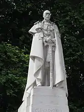 Statue en pierre blanche représentant George V avec une cape et s'appuyant sur une épée.
