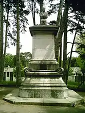 Photographie d'une statue : un petit buste posé sur un socle d'environ trois mètres de haut.