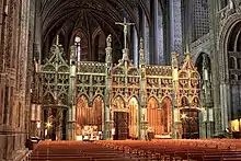 photo couleur d'un intérieur de cathédrale. Les murs peints de couleurs vives tranchent avec la blancheur et les dentelles de pierre du jubé qui coupe le volume transversalement.