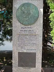 Photo couleur d'une stèle en granit poli incrustée d'un médaillon en bronze figurant le visage d'un homme. Une inscription en japonais proclame que « la culture doit primer sur la guerre ».