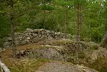 Tas de pierres indiquant un ancien mûr sur une colline rocheuse et boisée.